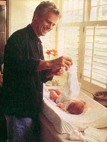 Richard Dean Anderson in a black shirt changing diapers of the infant Wylie Annarose.